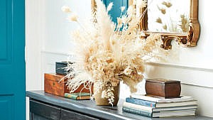 an organized hallway table with books and a vase of wild grass