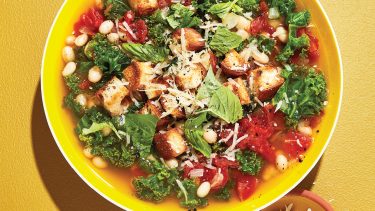 Soup with beans and kale in yellow bowl.