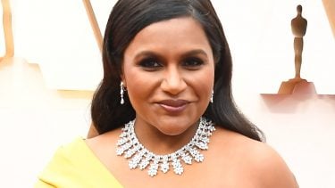 Mindy Kaling in a bright yellow one-shoulder chiffon gown and a diamond necklace.
