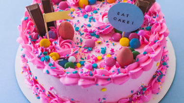 A pink cake covered in kit kats, chocolate eggs and sprinkles.