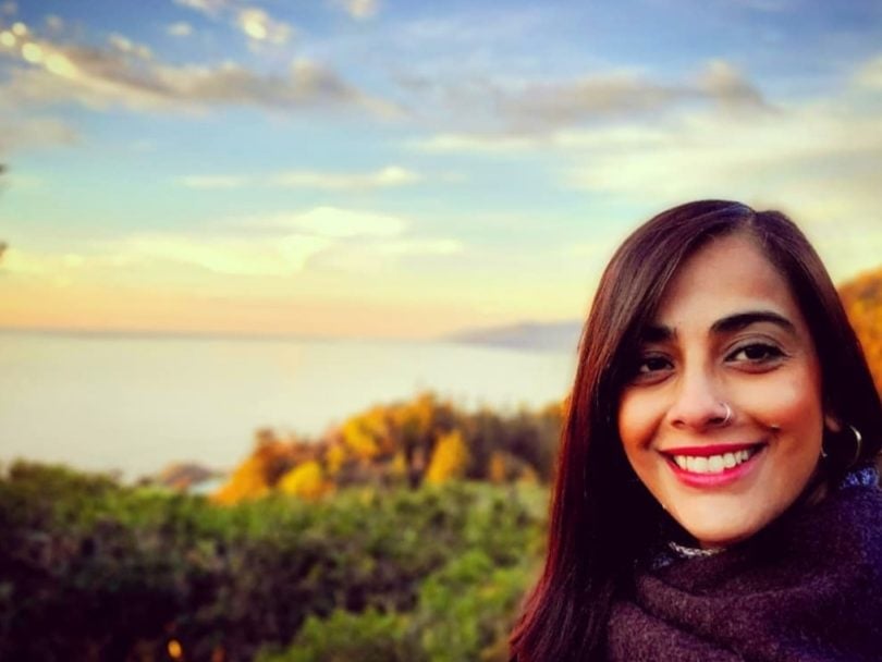 Charmaine Noronha smiling in front of a vista that includes trees and a lake.