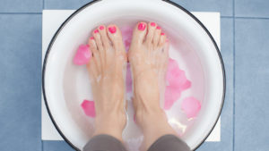 A person with nail polish on their toes soaking their feet in a foot bath with flower petals petals.