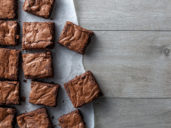 A grid of square-cut brownies on a sheet of waxed paper.