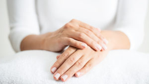 A woman's hands are shown propped up on a white towel to show off her gel nail polish manicure for an article on how to remove gel nail polish at home.