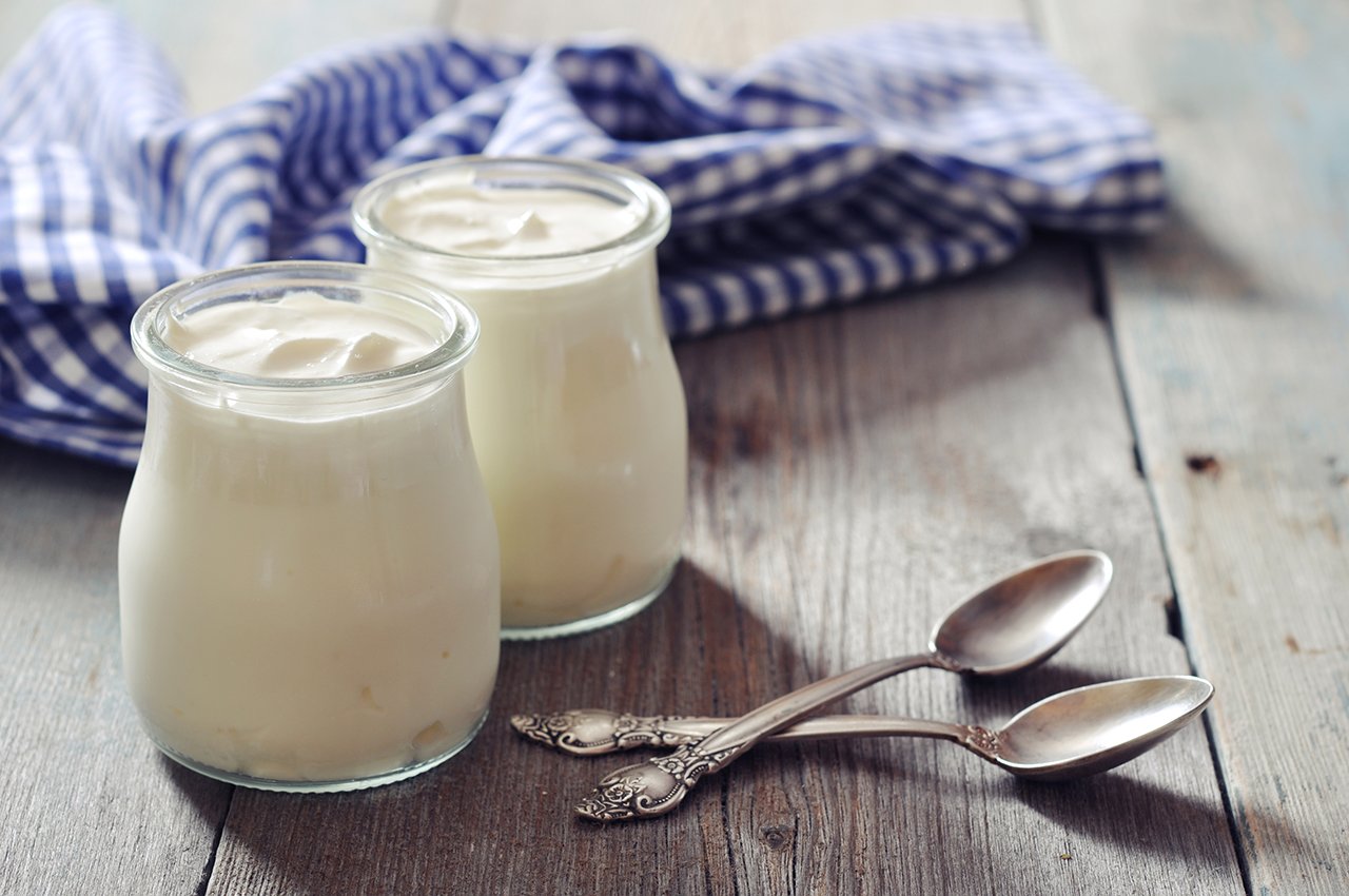 Homemade yogurt in glass jars with spoons on a wooden background