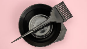 A mixing tray and brush on a pink background to illustrate an article on how to dye your own hair at home.
