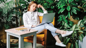 Woman sitting in plant-filled room with a desk and a laptop.