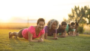 A group of adults attending a fitness class outdoors hold a plank position.