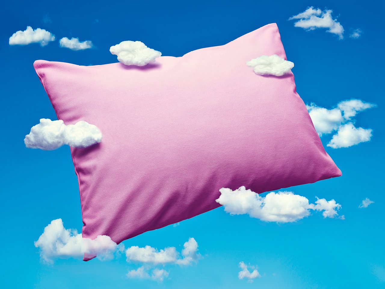 A photo illustration of a pink pillow floating through the clouds