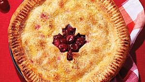 Sour cherry pie with maple leaf cut out, on a red background.