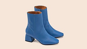 A pair of blue leather ankle boots from Maguire pictured against a pink background.