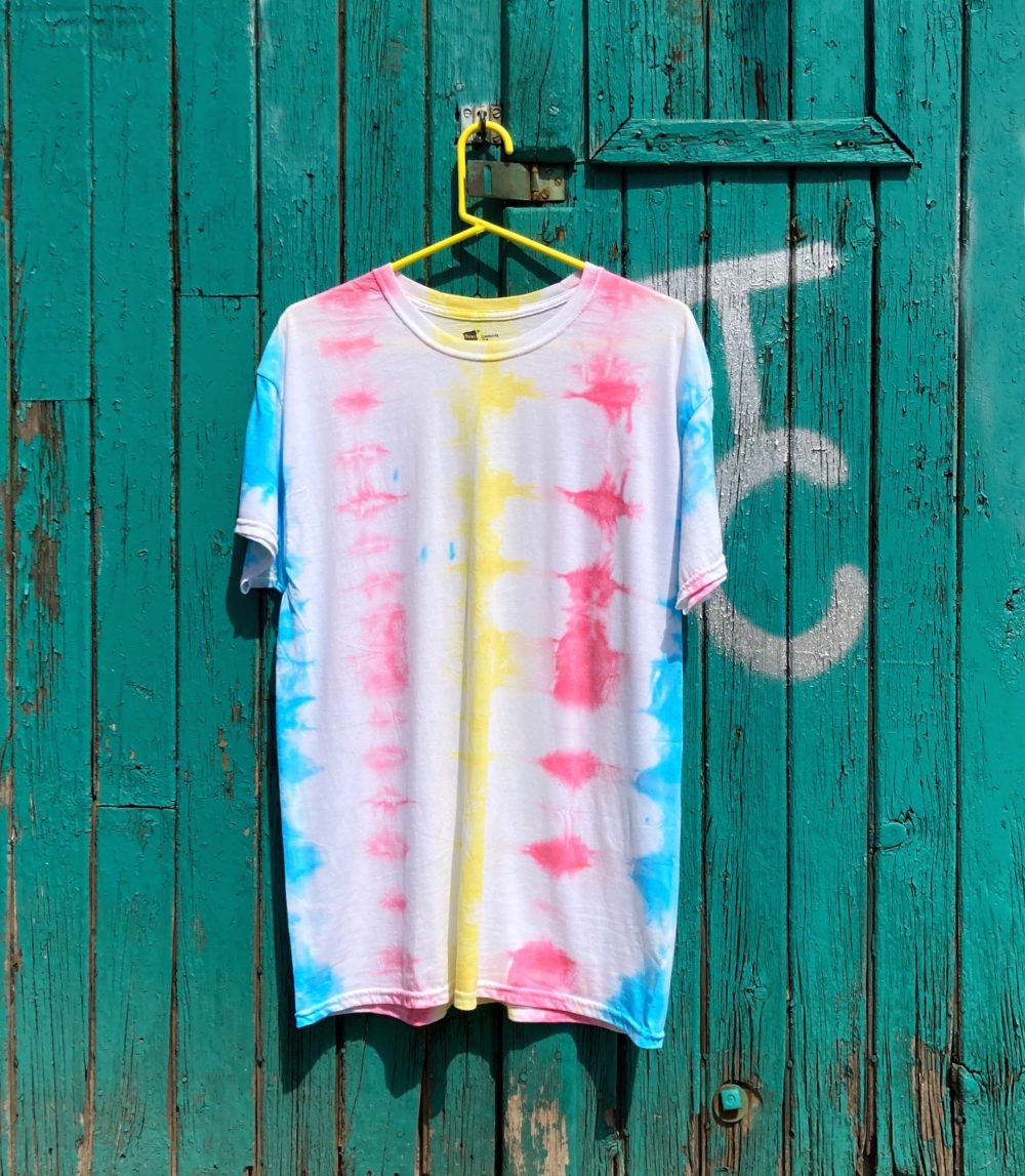 A pink, yellow and blue white tie-dyed shirt against a painted door