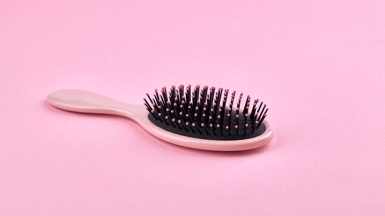 A pink hairbrush on a pink background for a piece on the 3 main reasons women might lose their hair