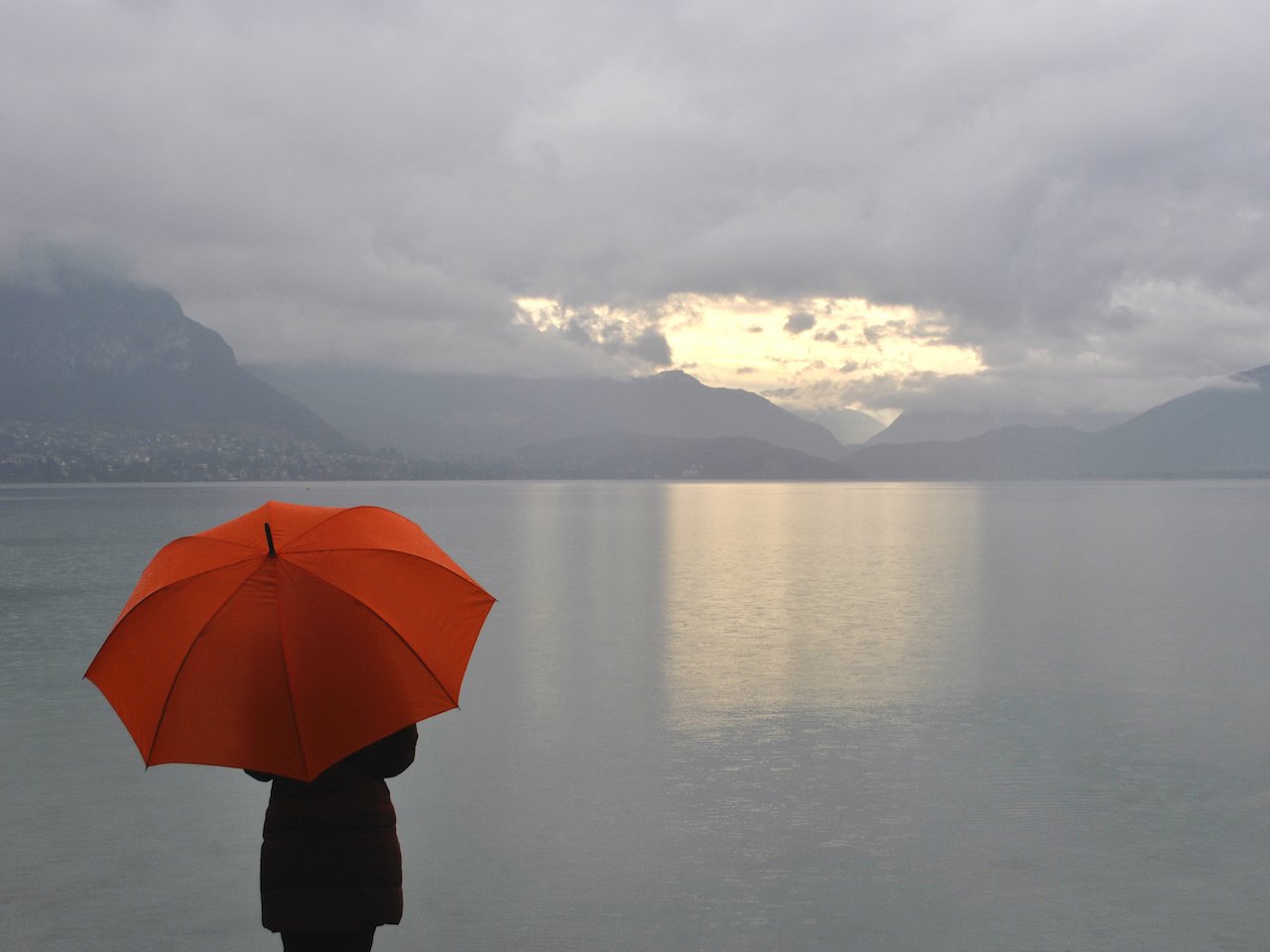 A woman under a red umbrella watches the sun rise through the clouds