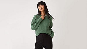 A model seen from the waist up wearing a green cotton Frank & Oak sweater.