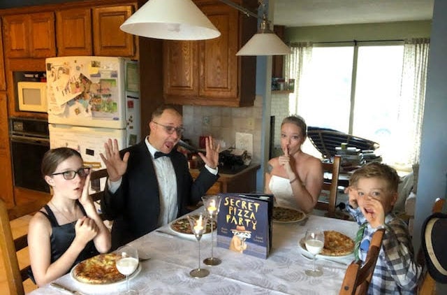 a man, woman, and two young children sit around a table with dinner plates and pizza