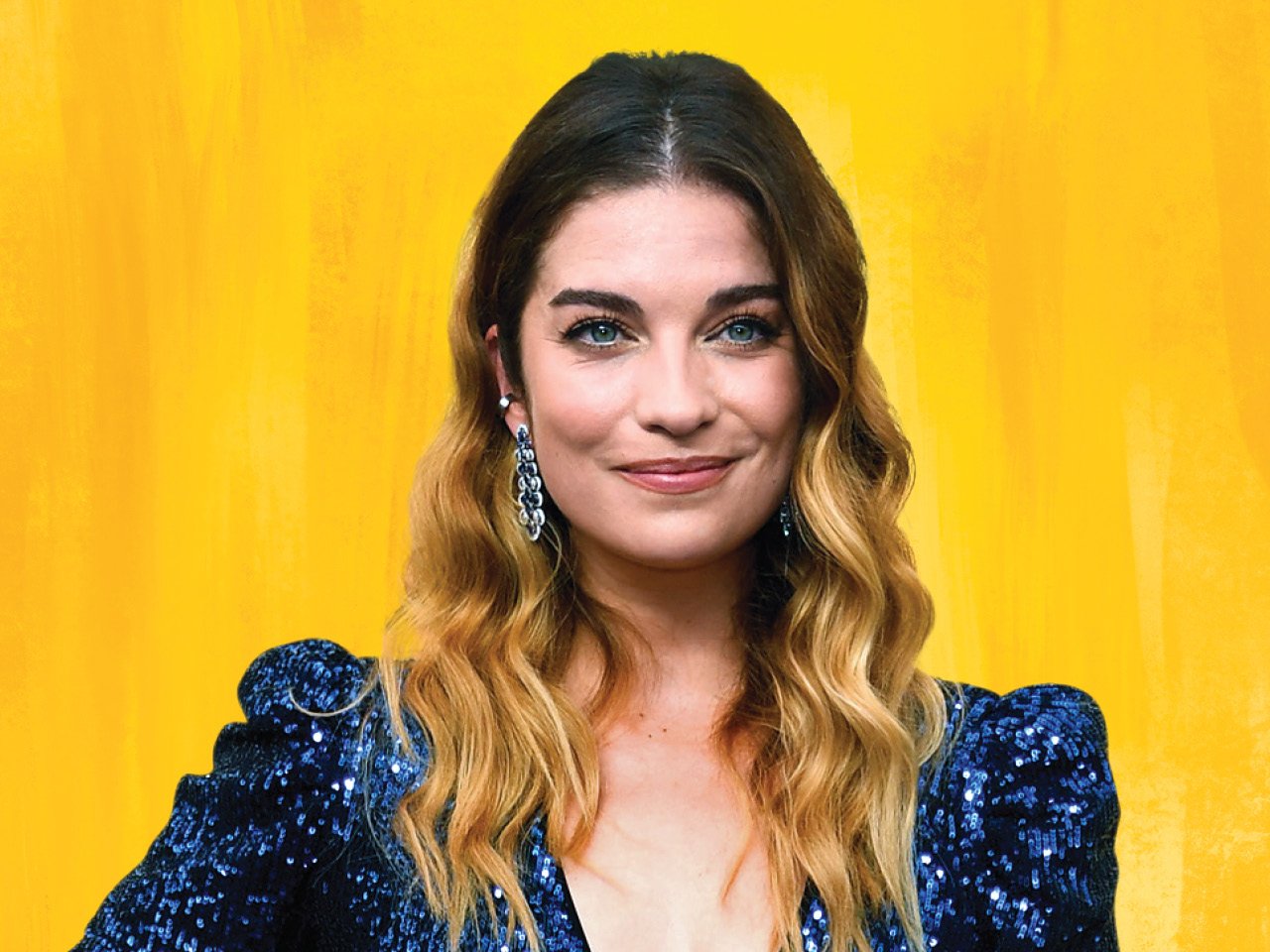 A photo of actor Annie Murphy in a blue sequinned dress on a yellow backdrop