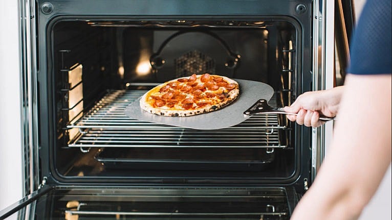 a pair of hands pull a freshly cooked pizza out of an oven with a pizza peel
