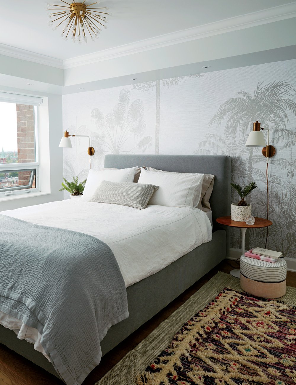 A queen bed with a dove grey fabric headboard against a wall with a grey and white removable mural.