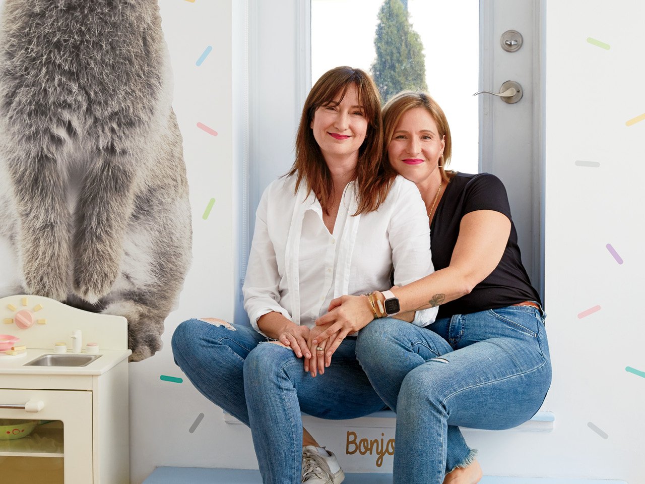 Two women sitting on a stoop in a child's bedroom. 