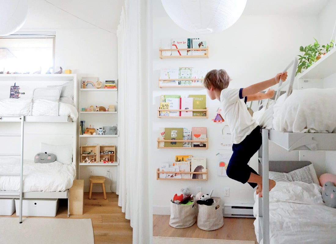White room with bunkbeds, and a kid hanging off of a bunkbed ladder.