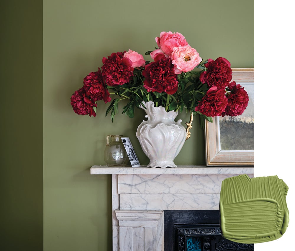 A bouquet of red and pink peonies in a white pitcher on top of a white mantel against a green wall