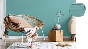 A photo of a natural brown Acapulco chair against a teal-y blue wall