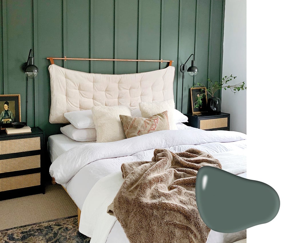 A photo of a bed with a brass frame against a blackened mineral green wall.