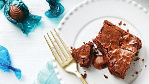 Chocolate brownie on white plate with boxed chocolates loose on tabletop