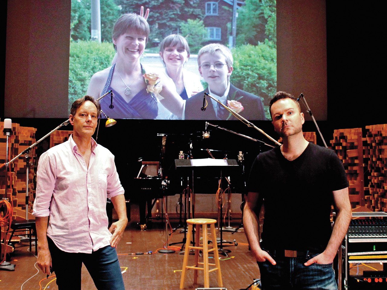 A photo of composer Jake Heggie, left, and Joshua Hopkins, in front of a photo of Hopkins' sister Natalie with her children.