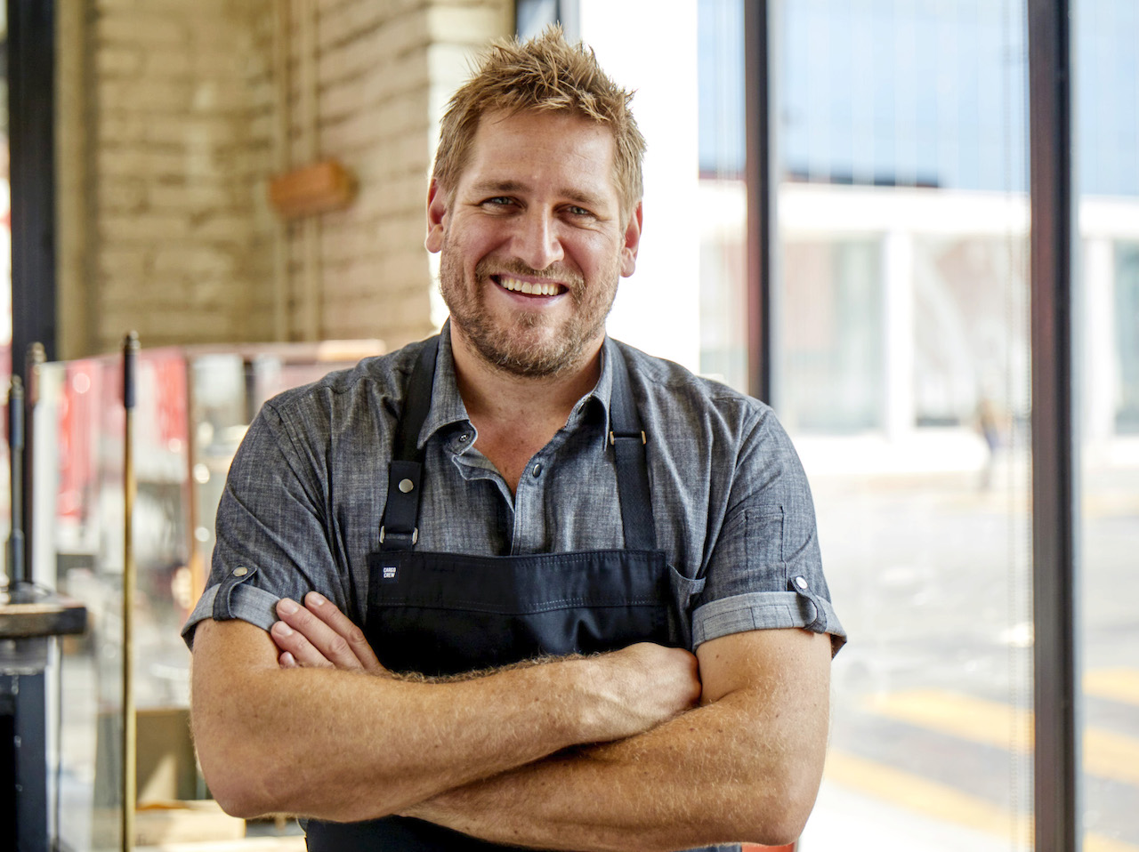 A photo of Chef Curtis Stone in a chambray short-sleeve shirt and navy apron