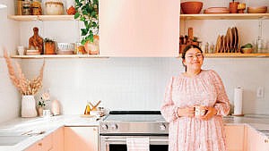 A woman in a pink dress standing in a pink kitchen to illustrate an article about easy DIY paint projects.
