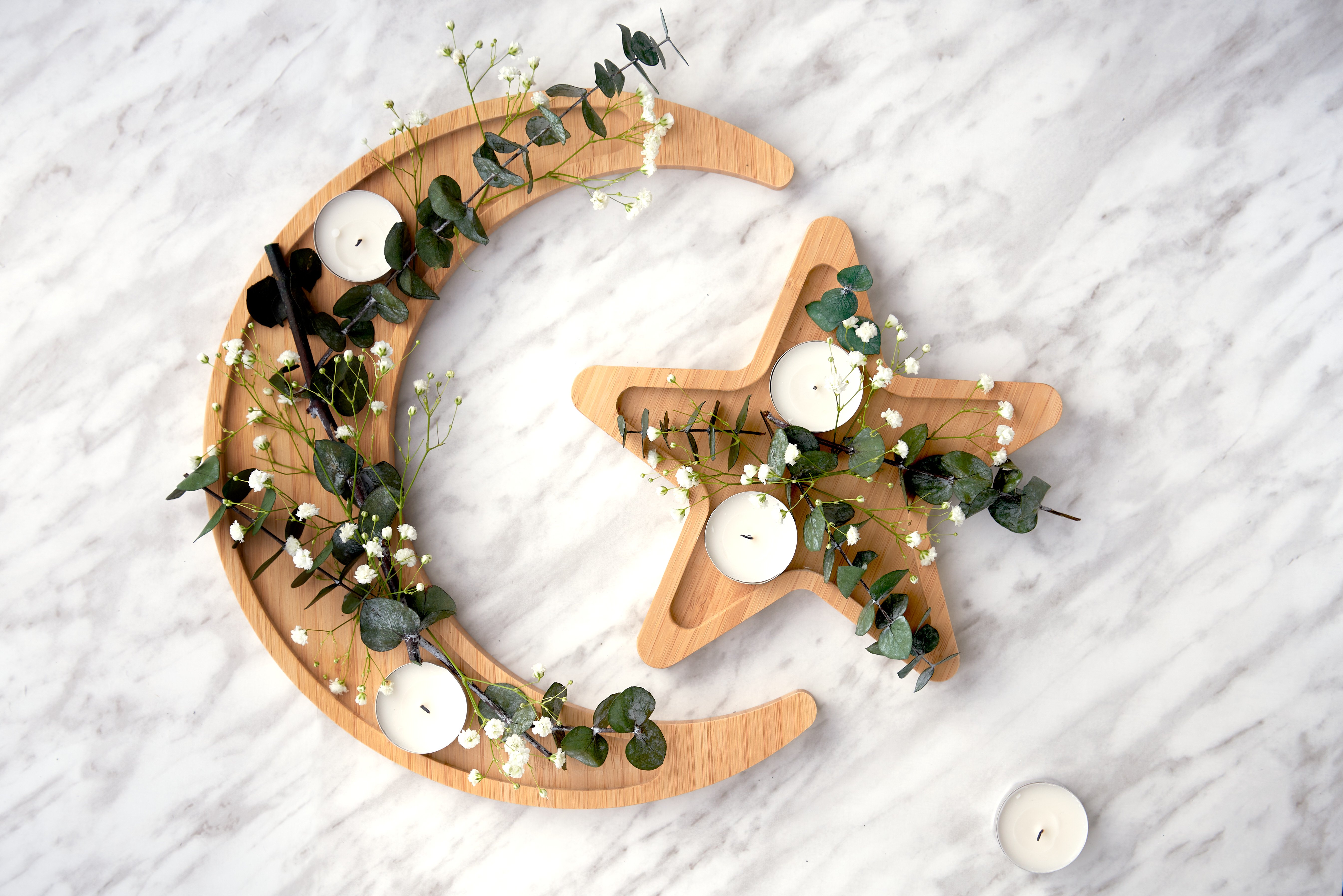 A moon and star bamboo wood platter with candles and green twigs rests on a white countertop