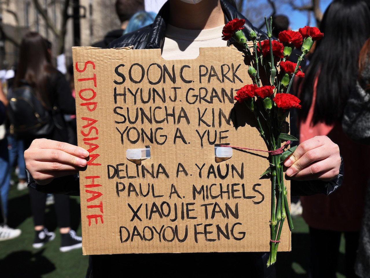 A woman holds up a sign with the names of the Atlanta shooting victims and a bunch of red flowers at a rally against hate in Columbus Park on March 21, 2021 in the Chinatown neighborhood of Manhattan in New York, New York. A rally for solidarity was organized in response to a rise in hate crimes against the Asian community since the start of the coronavirus (COVID-19) pandemic in 2020. On March 16 in Atlanta, Georgia, a man went on a shooting spree in three spas that left eight people dead