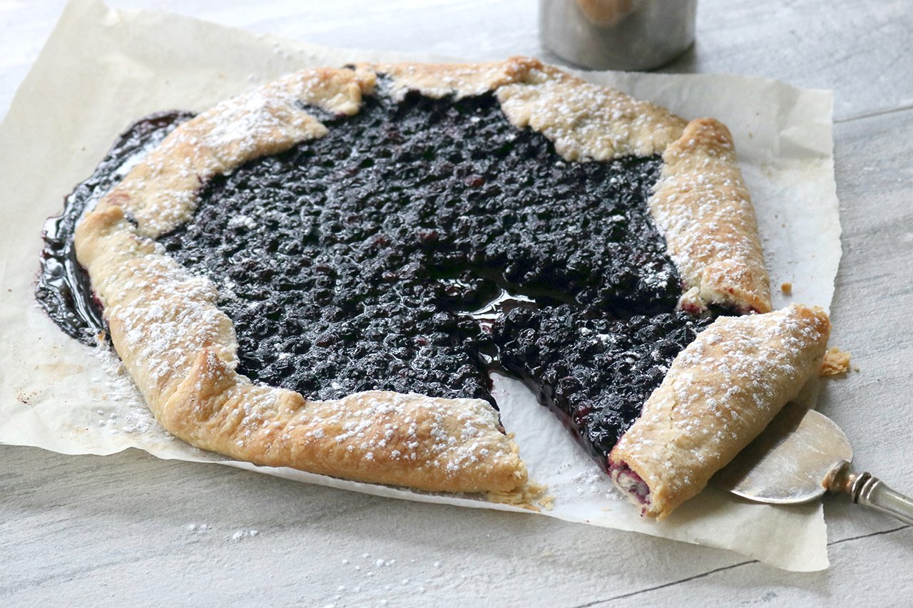 A Vegan Blueberry Galette with a slice cut out of it and a server underneath