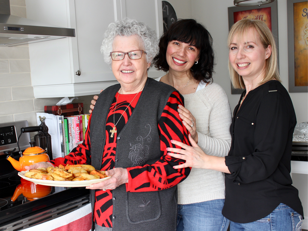 three women stand in kitchen holding food