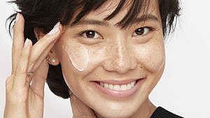 A woman applying face cream for an article on peptides as a skincare ingredient.
