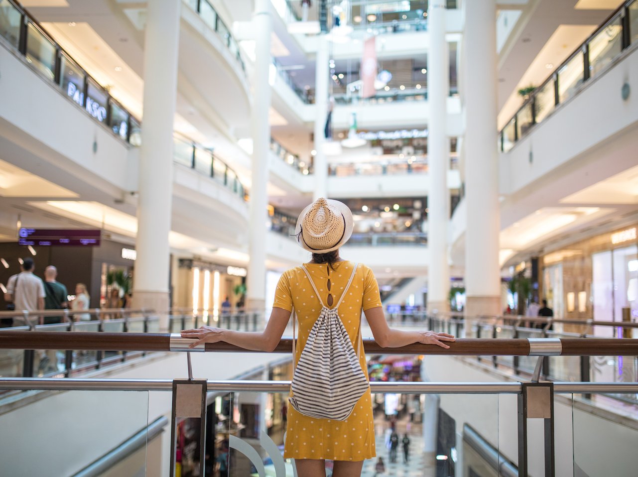 A woman standing on a balcony at a shopping mall, looking out at the mall