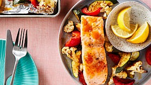 one-pan roasted salmon and vegetables on a plate with two lemon wedges