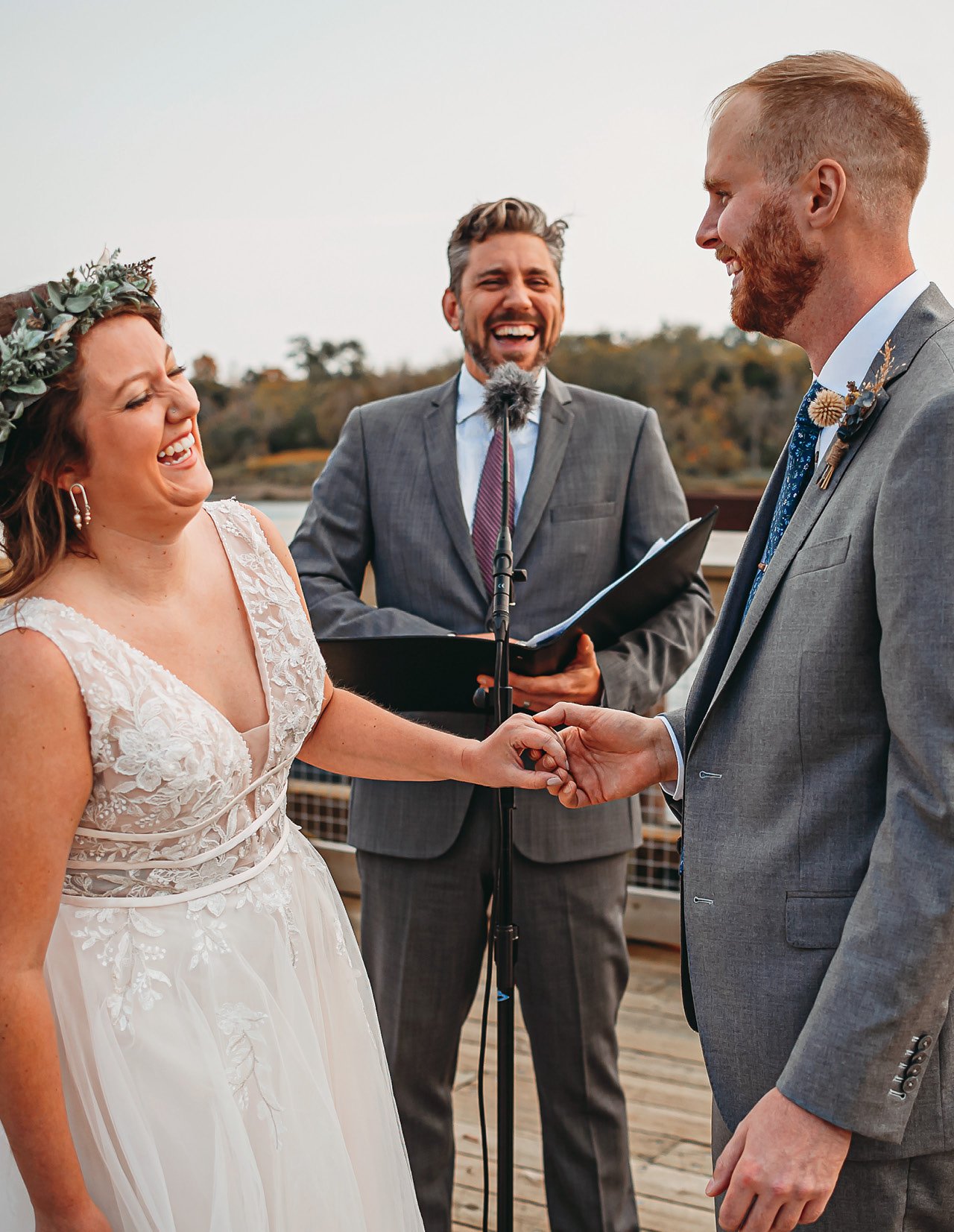 A photo of a bride and groom and their officiant on a dock, all laughing