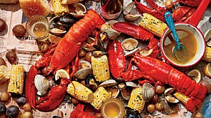 Lobster, clam, mussels, corn cobs, potatoes and beer on top of newspaper