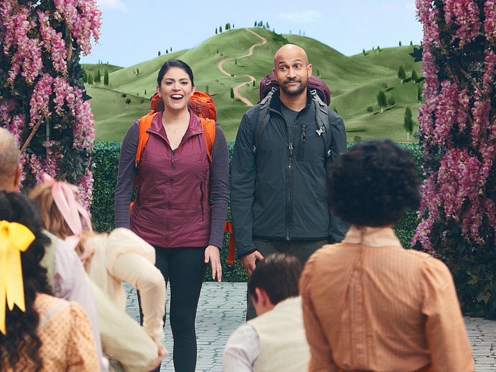 Cecily Strong and Keegan-Michael Key wearing backpacks on a set in front of a mountain on the tv show Schmigadoon!