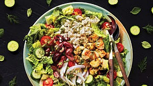 A plate of greek chicken salad with a fork and spoon at the side