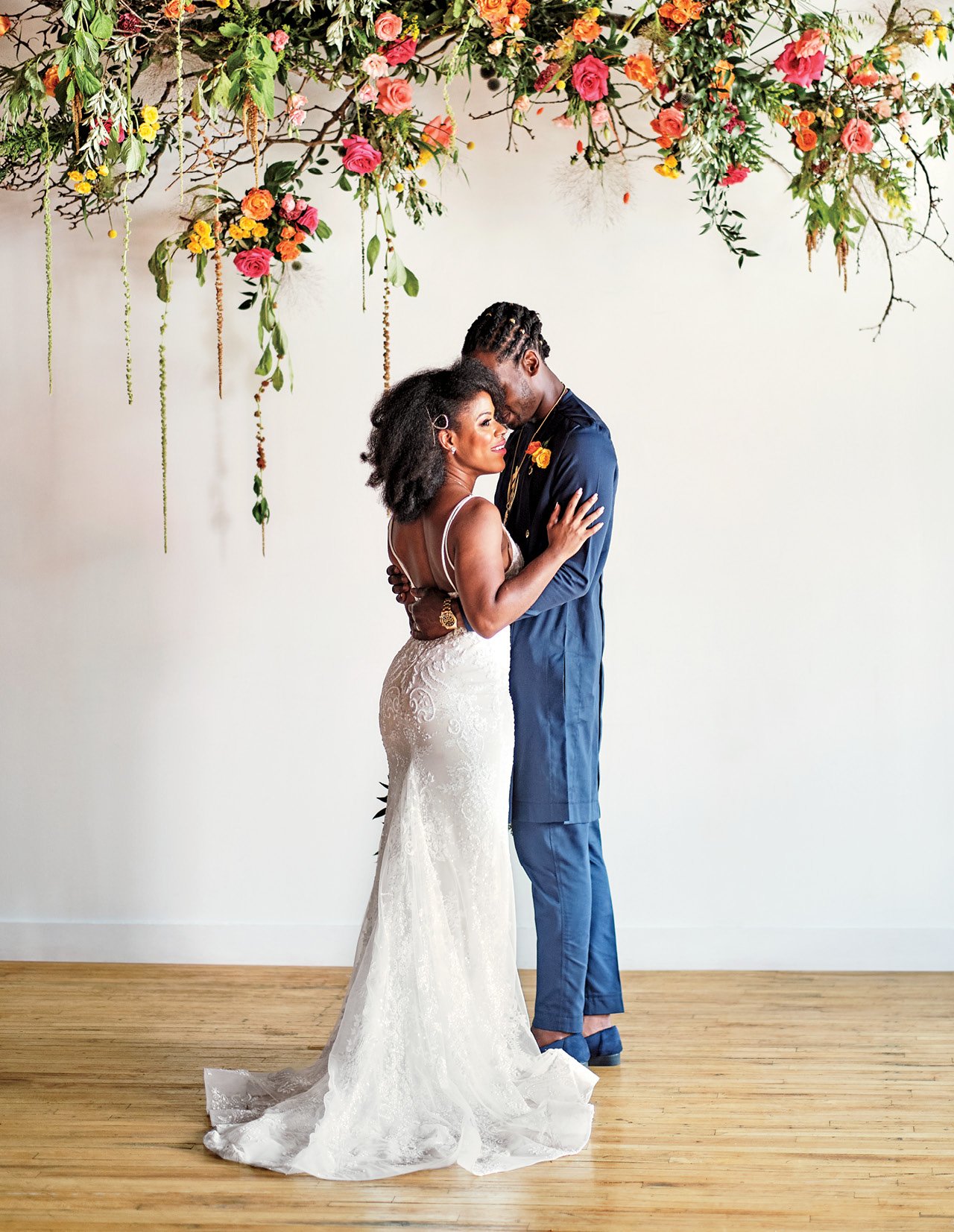 A newlywed Black couple embrace under a floral installation