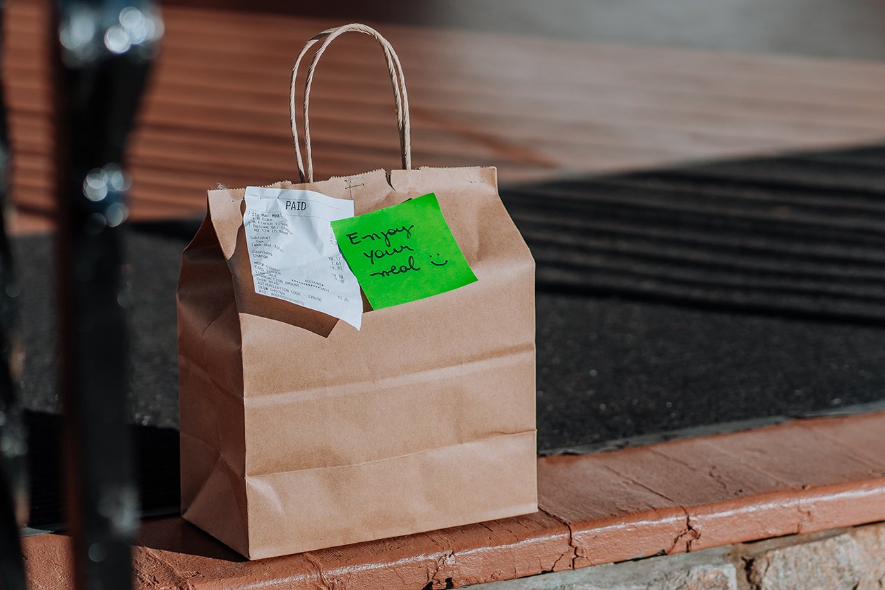 A brown paper bag of takeout food with a note that reads "enjoy your meal"