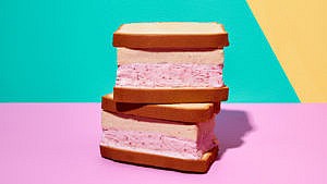 Strawberry ice cream and peanut butter ice creams sandwiched between two pound cakes stacked on top of each other in front of a turquoise and pink background