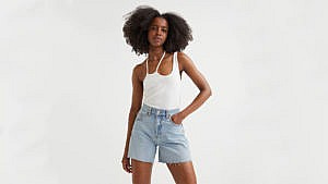 A model wears a pair of light wash high-waisted denim shorts and a white tank top.