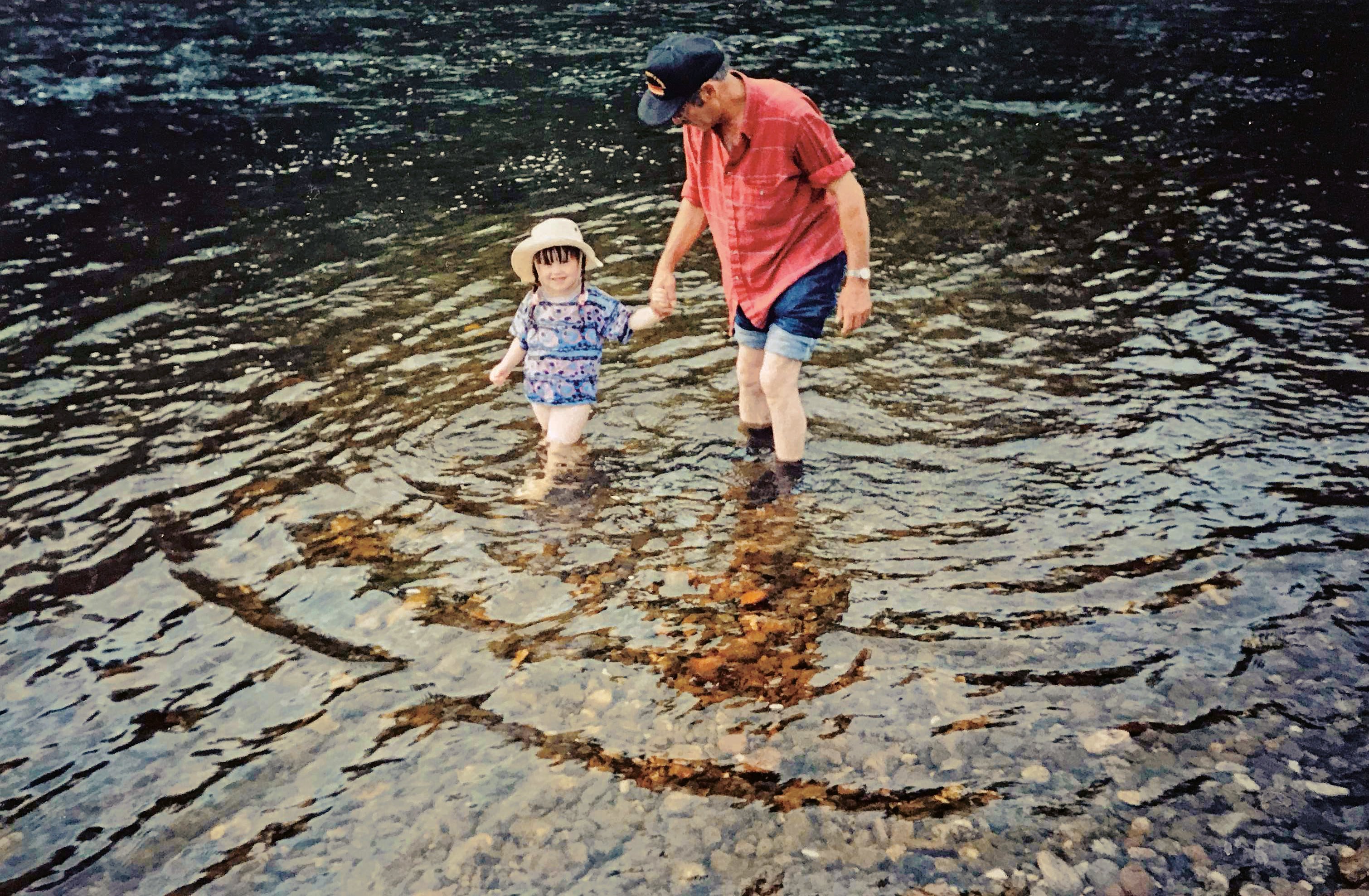 A man and child hold hands and wade in a river