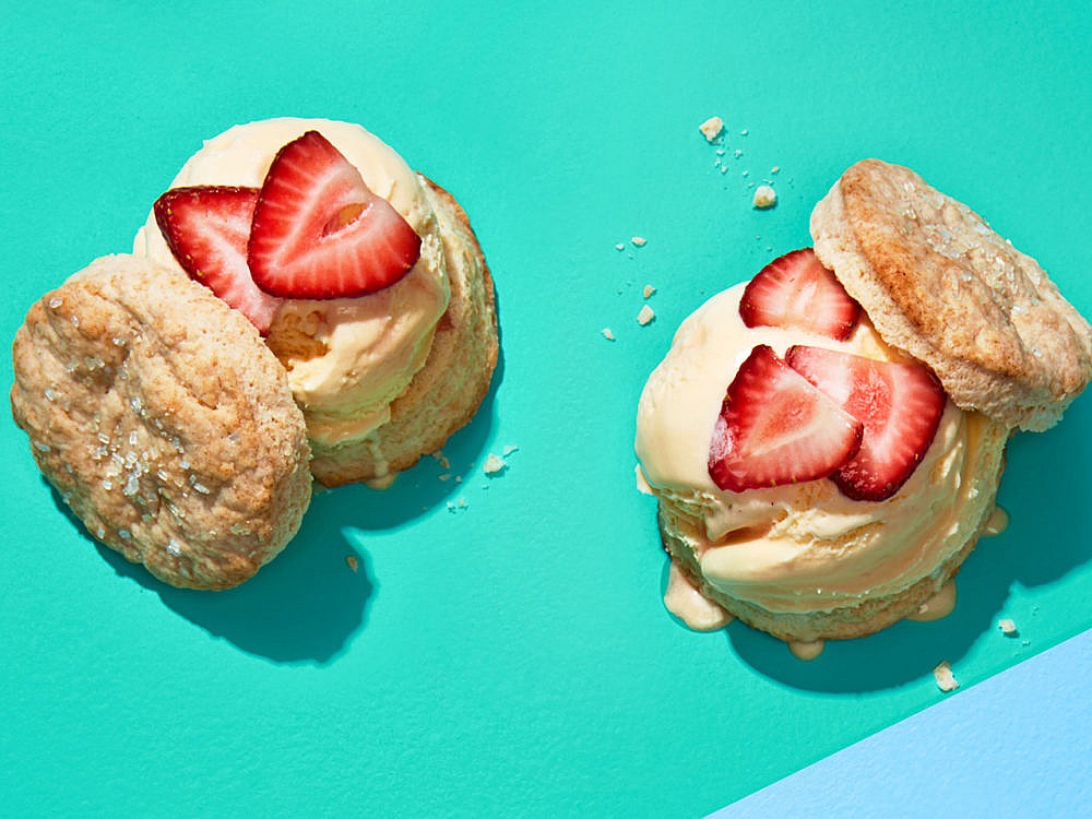 Two mascarpone ice cream scone-wiches topped with sliced strawberries on a green background