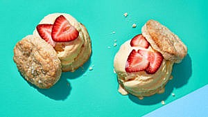 Two mascarpone ice cream scone-wiches topped with sliced strawberries on a green background